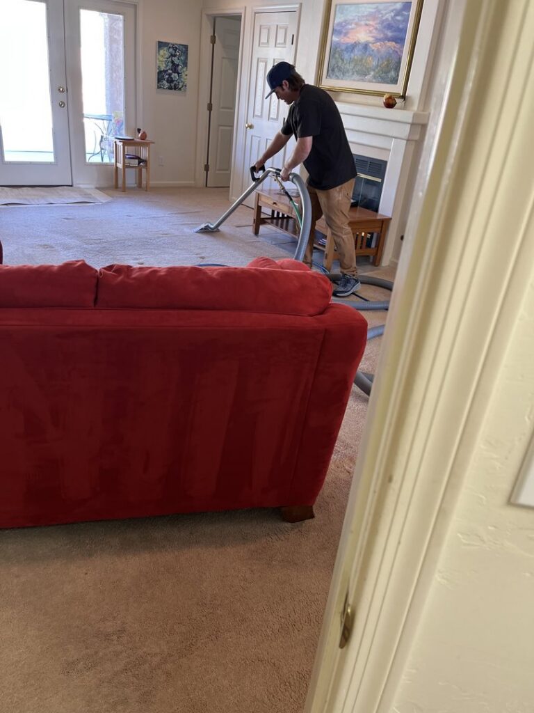 A professional cleaning a living room carpet with a cleaning wand, provided by Soft N Dry in Tucson, AZ.
