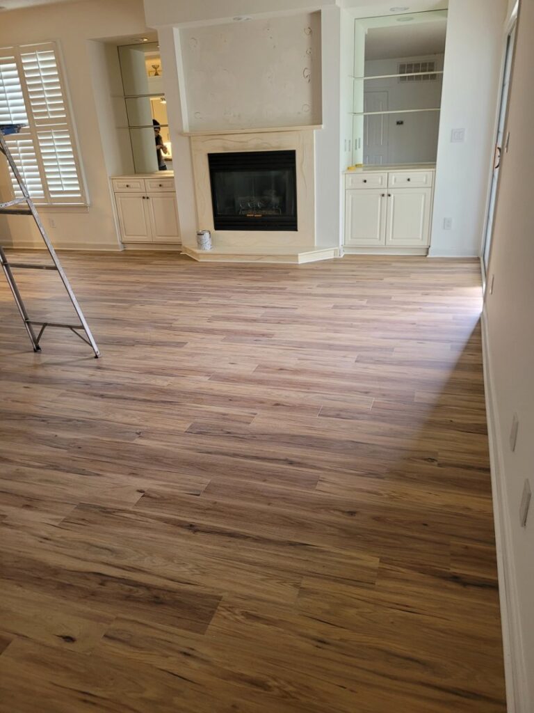 A living room with a fireplace and newly installed wood-look flooring by VA Carpet Connection LLC in Chesapeake, VA.