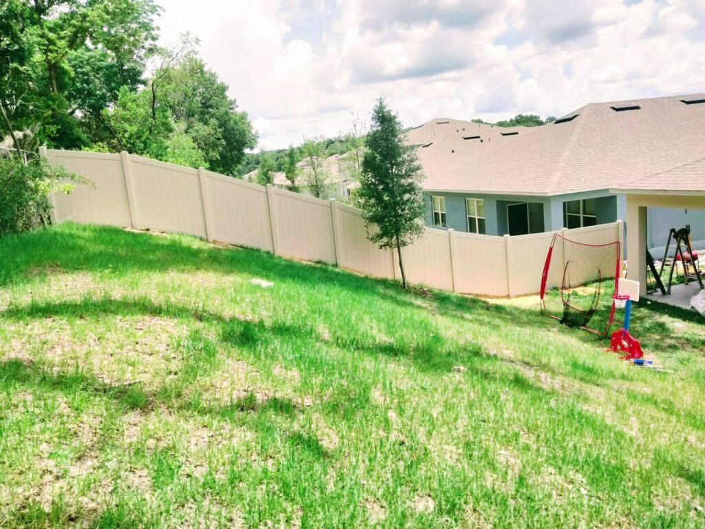 A long beige vinyl fence installed on a sloped residential backyard by Florida Professional Fence LLC in Altamonte Springs, FL.