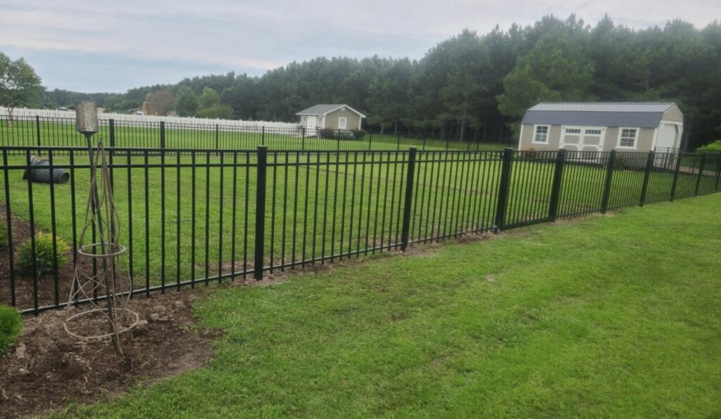 A long newly installed black aluminum fence enclosing a backyard with sheds by Fast Fence LLC in Bradenton, FL.