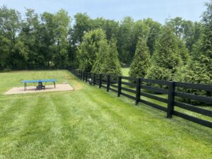 A long black wooden fence installed in a spacious backyard with trees, by Pileggi Fence Painting in Franklin, TN