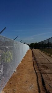 A long chain-link fence with barbed wire at the top, installed along a path by Life Time Fence, Inc. in Cedar Rapids, IA.