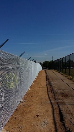 A long chain-link fence with barbed wire at the top, installed along a path by Life Time Fence, Inc. in Cedar Rapids, IA.