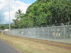 A long chain-link fence with barbed wire installed along a road by David's Fencing Inc. in Waipahu, HI.