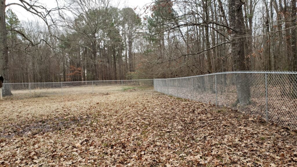 A long chain-link fence extending through a wooded area by Fences & Landscape Inc in Little Rock, AR.