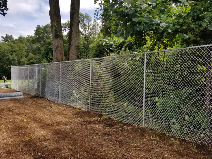 A long chain-link fence providing security and demarcation in a wooded area, installed by Fox Fence Enterprises Inc in Clifton, NJ.