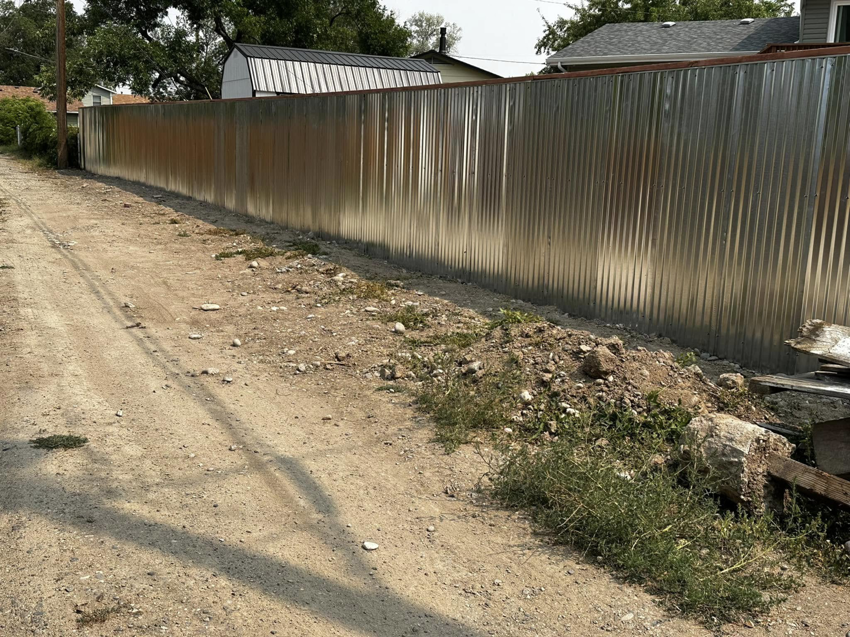 A long corrugated metal fence installed along a dirt path by Tomahawk Fencing in Riverton, WY.