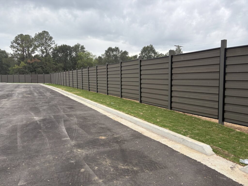 A long dark horizontal slat fence installed along a parking lot by Jefcoat Fence Co. Inc. of Hattiesburg, MS
