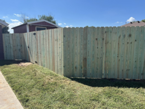 A long green-treated wooden fence with a gate providing privacy for a home by Timber Wolf Fence Co. in Rogers, AR.