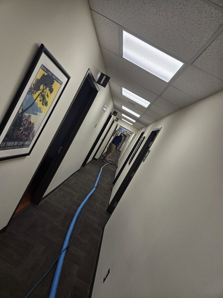 Long hallway carpet cleaning in progress with equipment and hoses by On The Spot Carpet and Upholstery Cleaning in Warren, MI.