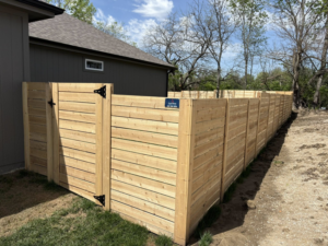 A long section of newly installed horizontal slat wooden fence with a gate by Fry's Fence LLC in Grain Valley, MO.