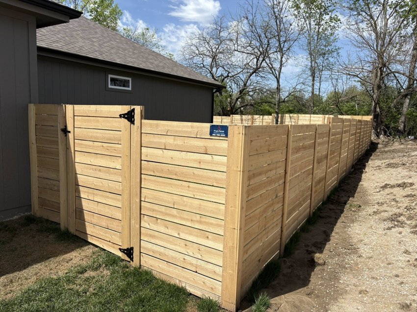 A long section of newly installed horizontal slat wooden fence with a gate by Fry's Fence LLC in Grain Valley, MO.