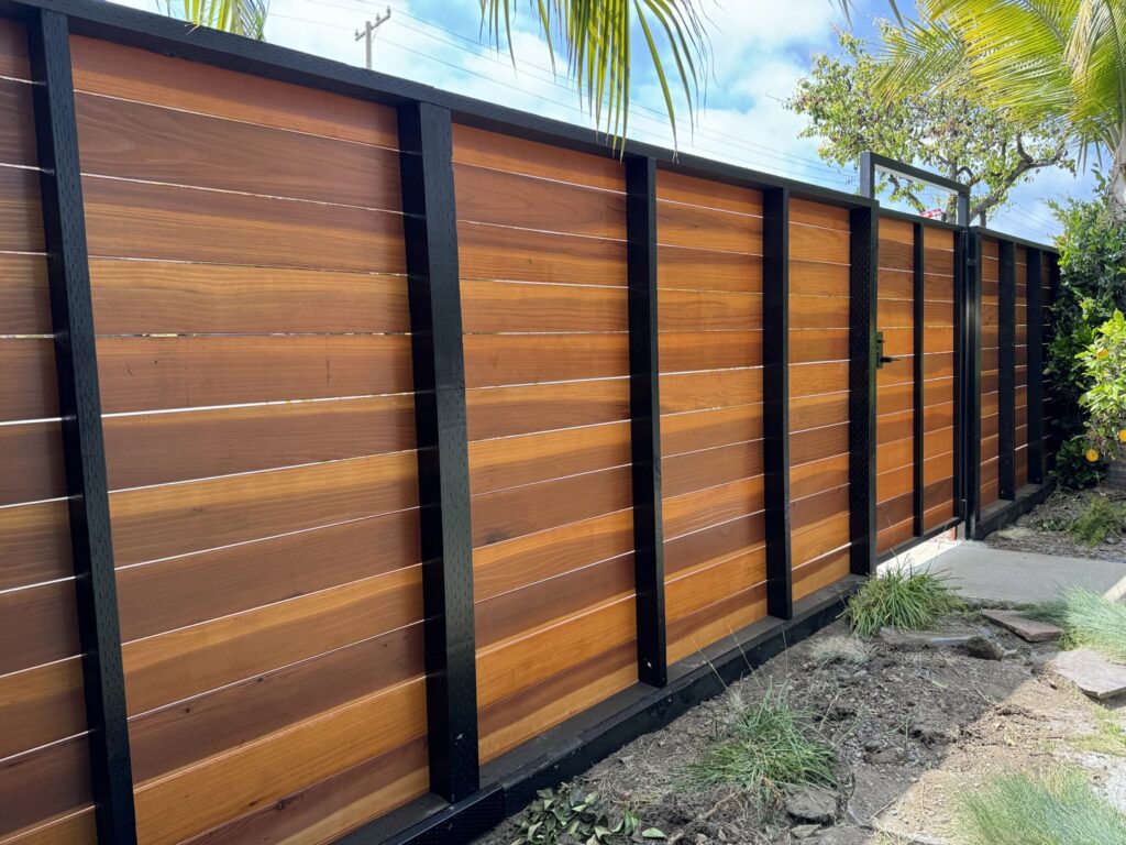 A long modern wood fence with black metal posts and a matching gate, installed by Harwell Fencing & Gates Inc. in Los Angeles, CA.