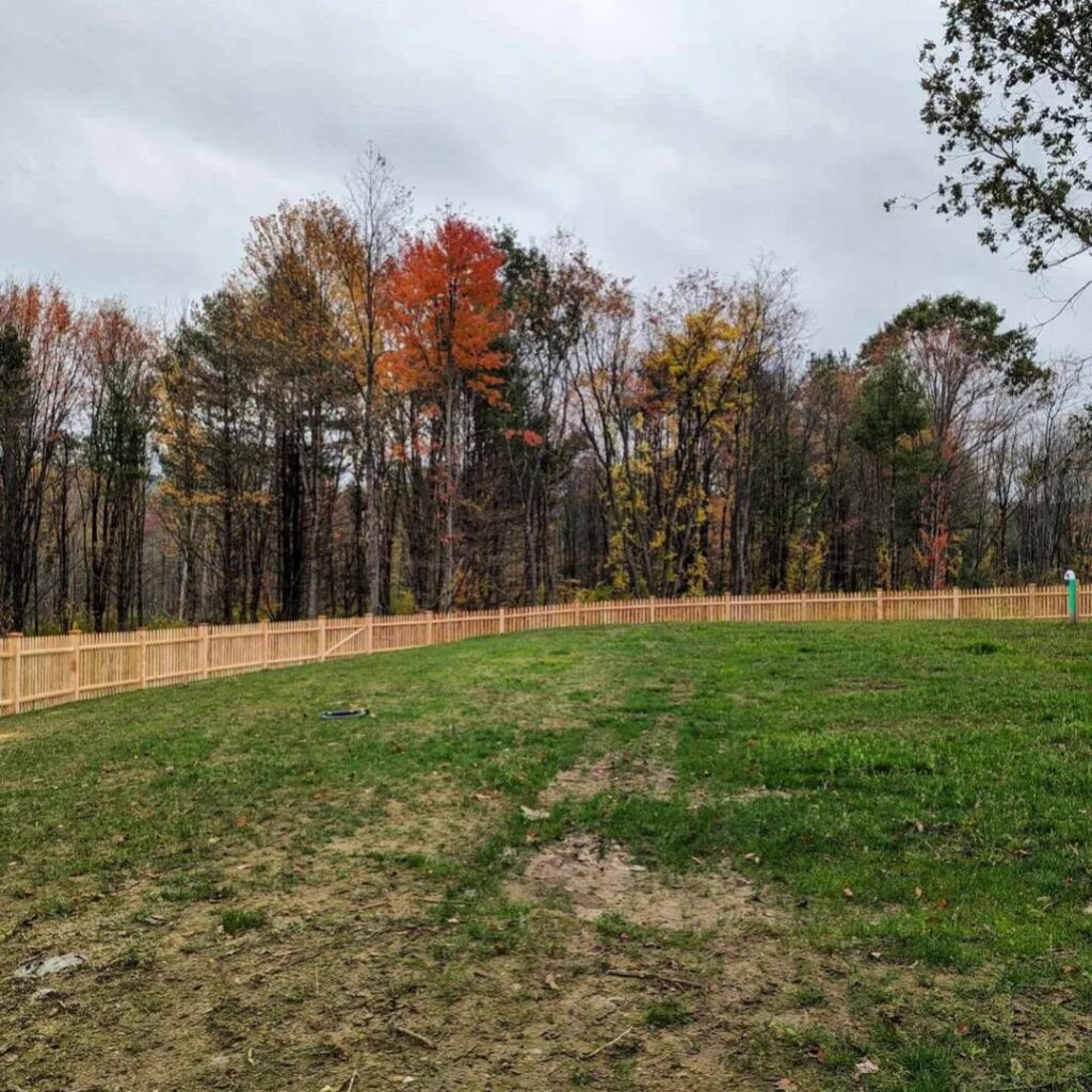 A long natural wood picket fence stretching across a large grassy field by Precision Fence NH in Hooksett, NH.