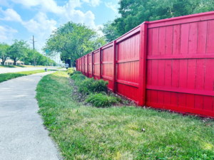 A long, newly painted red wooden privacy fence installed alongside a sidewalk by HammerHorn Fence & Gate Systems in Rochelle, IL.