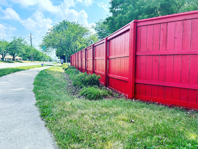 A long, newly painted red wooden privacy fence installed alongside a sidewalk by HammerHorn Fence & Gate Systems in Rochelle, IL.