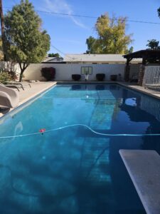 A long residential pool with a pool cleaner hose in the water by Vanguard Pool Care in Phoenix, AZ