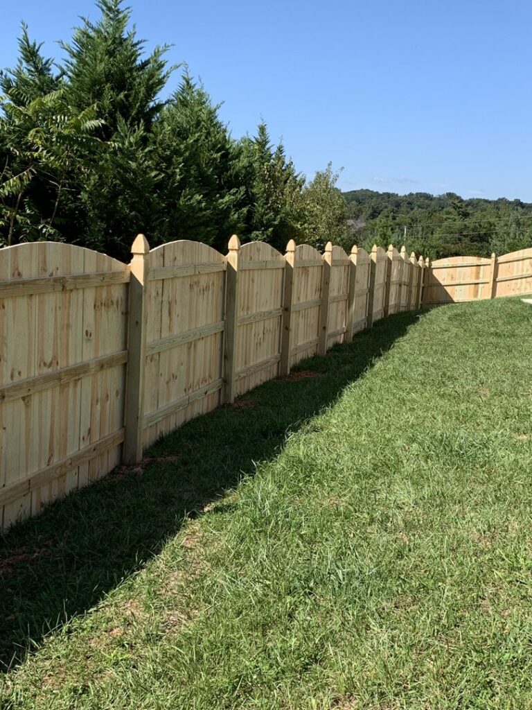 A long scalloped wood privacy fence on a grassy slope by Escamilla Fence Co. in Knoxville, TN
