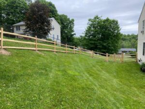 A long split rail fence with wire mesh and a gate installed on a sloped residential yard by Flanagan Fencing in Brookfield, CT.
