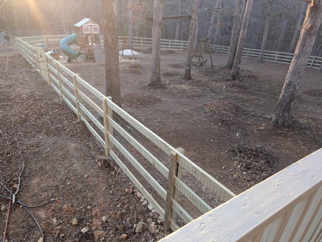 Extensive wooden split-rail fence with wire mesh enclosing a backyard with a playset, installed by Sunrise Fences in Goose Creek, SC.