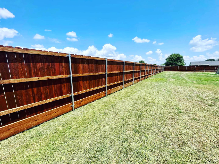 A long stretch of newly installed dark stained wooden privacy fence with metal posts by HammerHorn Fence & Gate Systems in Rochelle, IL.