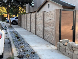 A long stone-texture concrete fence with a modern wooden gate by StackWall Manufacturing in Pomona, CA.