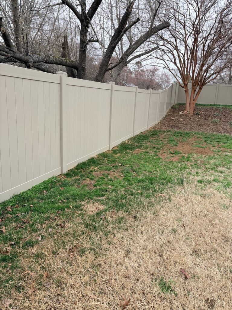 A long tan vinyl privacy fence installed along a property line by Outsiders Fencing in Greensboro, NC.
