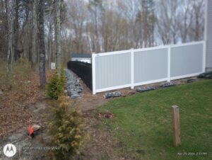 A long section of two-tone white and grey vinyl fence installed on a sloped property by Reilly Fence Inc in Cranston, RI.