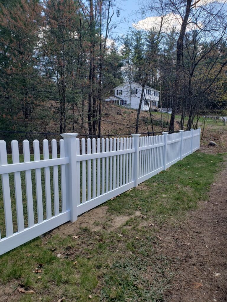 A long, classic white picket fence defining a property line, expertly installed by Sullivan & Sons Fence LLC in Hudson, NH.