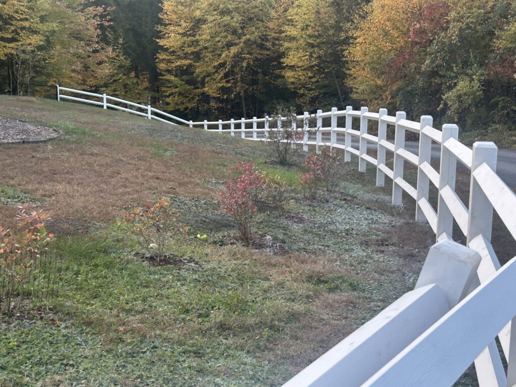 A long white split-rail fence gracefully following the contour of a hill by Precision Fence NH in Hooksett, NH.