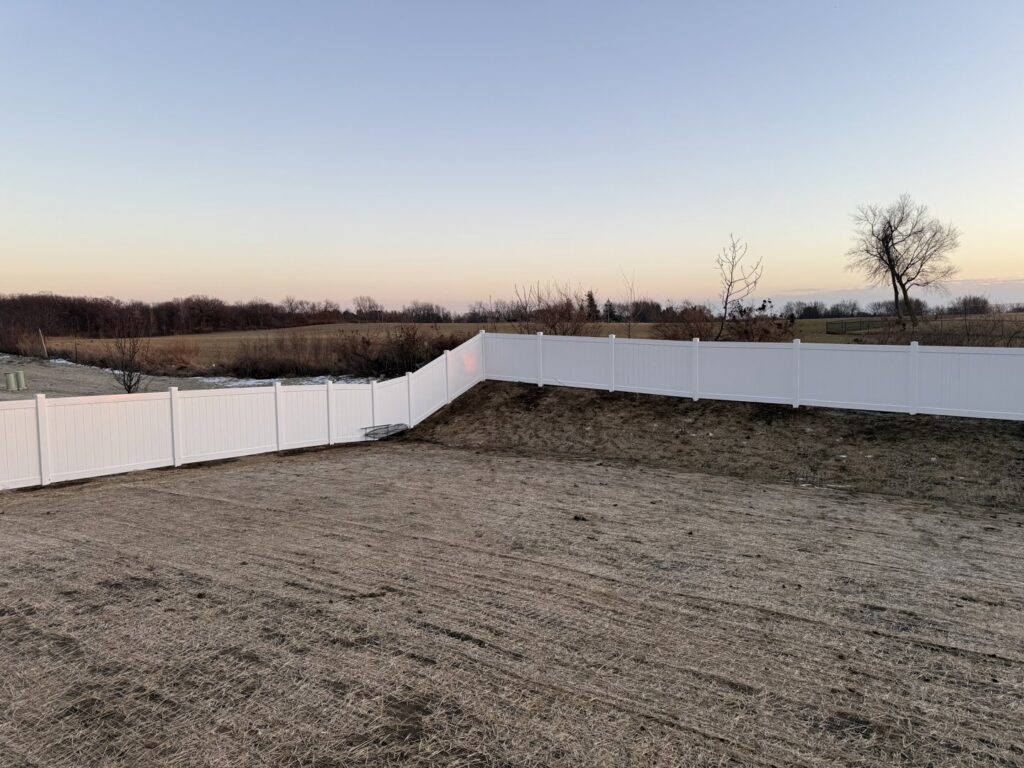 A long white vinyl fence installed in a residential backyard by Fence Connection, Inc. in Elgin, IL.