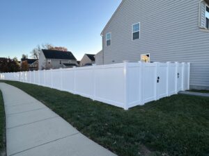A long stretch of newly installed white vinyl privacy fence running alongside a sidewalk by AFK FENCE LLC in Waldorf, MD.