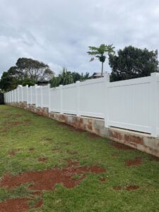 A long white vinyl fence installed on a concrete block retaining wall by Redmond Valleywide - Hawaii's Fence Company in Kapolei, HI