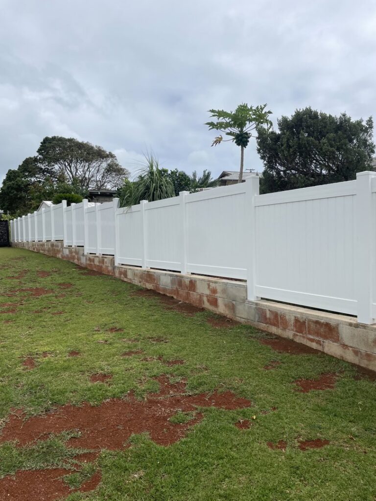 A long white vinyl fence installed on a concrete block retaining wall by Redmond Valleywide - Hawaii's Fence Company in Kapolei, HI