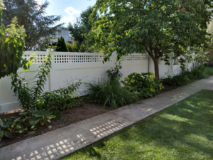 A long white vinyl fence with a decorative lattice top installed along a garden and sidewalk by Low-Level Construction LLC in York, PA.