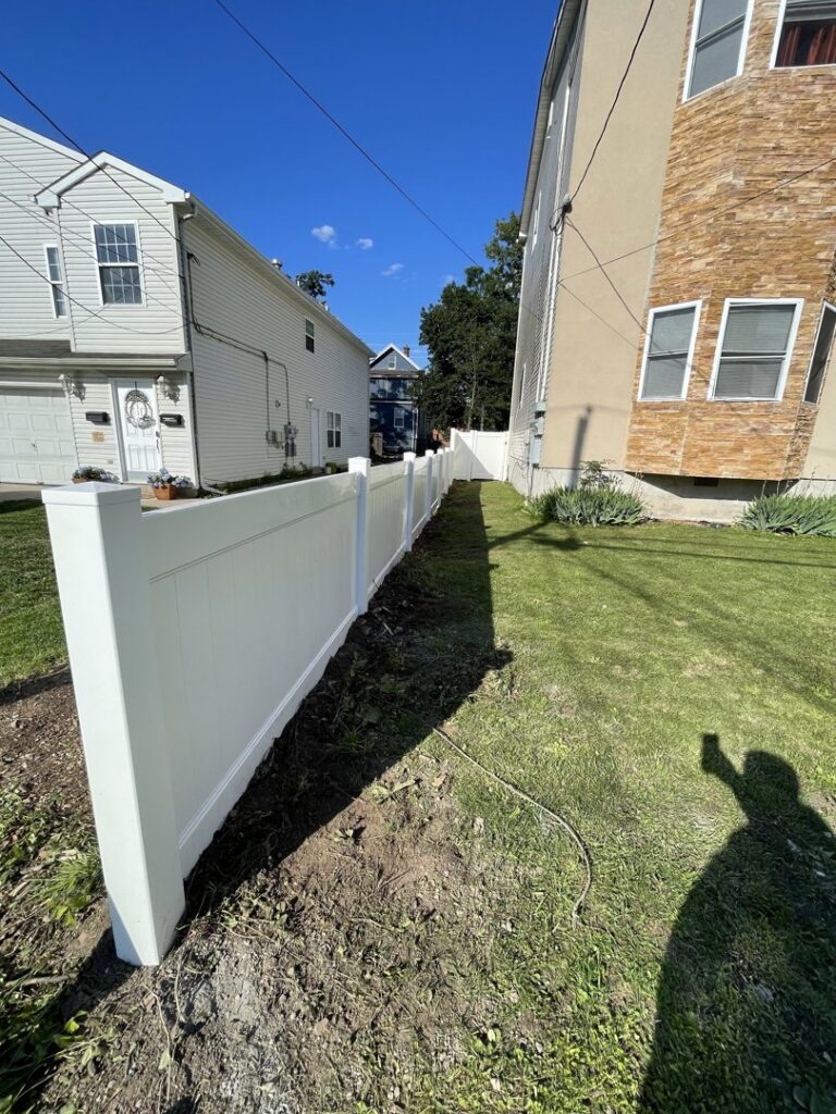 A long white vinyl fence installed along a property line by Brothers Fence in Elizabeth, NJ.