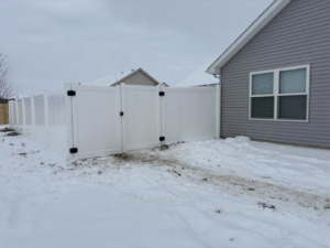 A long white vinyl privacy fence with a gate installed around a residential property by H&M Fencing LLC in Decatur, IN.