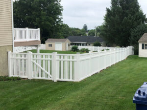 A long white vinyl picket fence with a gate installed around a backyard by Hitz Fence in Lebanon, PA.