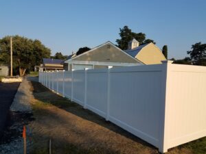 A long white vinyl privacy fence installed next to a paved area by 802 Fence Company LLC in Shoreham, VT.