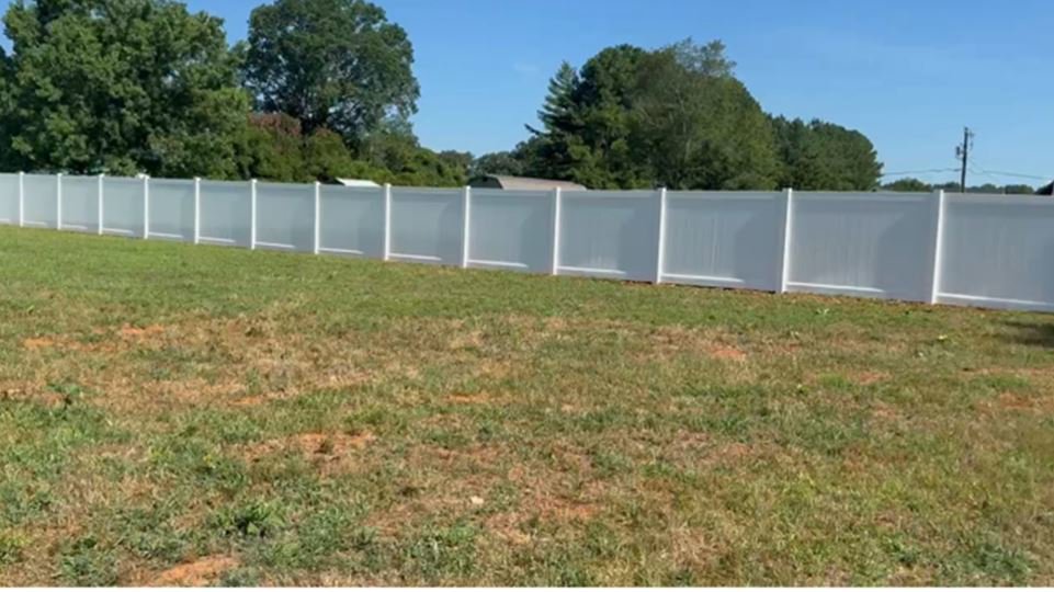 A long, clean white vinyl privacy fence installed in a spacious field by Cavitt Fencing in Concord, NC.