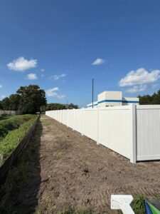 A long newly installed white vinyl privacy fence along a dirt path near a commercial building by Fast Fence LLC in Bradenton, FL.