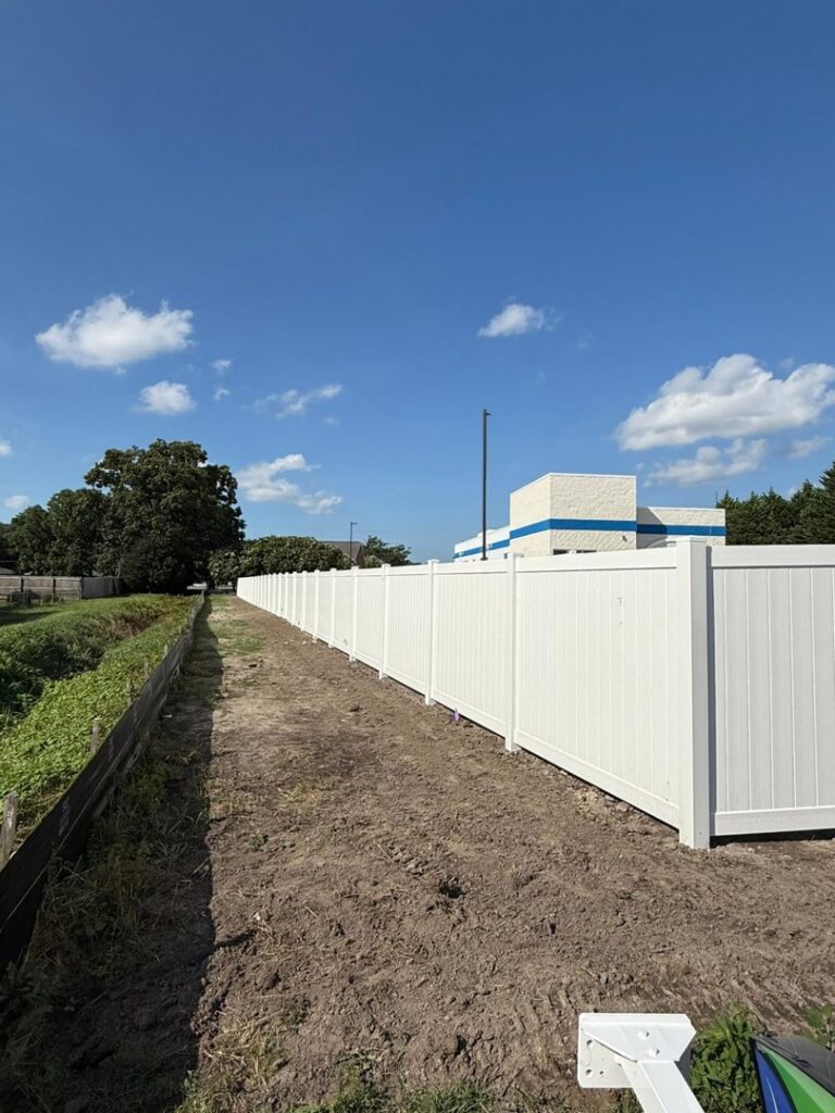 A long newly installed white vinyl privacy fence along a dirt path near a commercial building by Fast Fence LLC in Bradenton, FL.