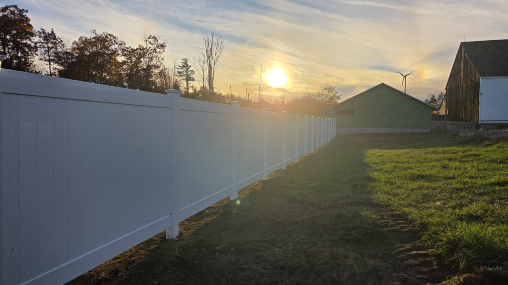 A long white vinyl privacy fence installed in a spacious yard by Creative Fence in Casco, ME.