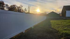 A long white vinyl privacy fence installed in a spacious yard by Creative Fence in Casco, ME.