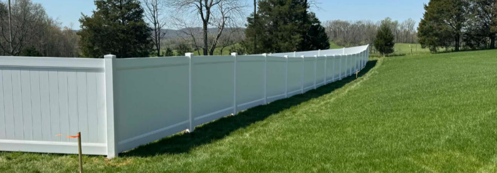 A long white vinyl privacy fence installed in a green field by KY Fencing Unlimited in Louisville, KY.