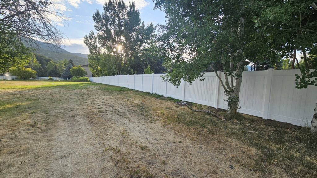 A long white vinyl privacy fence installed in a spacious rural setting by All American Vinyl in Provo, UT.