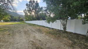A long white vinyl privacy fence installed in a spacious rural setting by All American Vinyl in Provo, UT.
