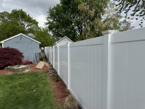 A long white vinyl privacy fence installed along a property line by Texeira Fencing & Concrete in Springfield, MA.