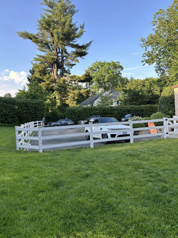 A long white wood and wire mesh fence bordering a driveway and lawn by Building Fences in Westchester NY.