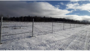 A long wire mesh fence with a gate extending across a snowy field, installed by Doolan Fence in Montpelier, VT.